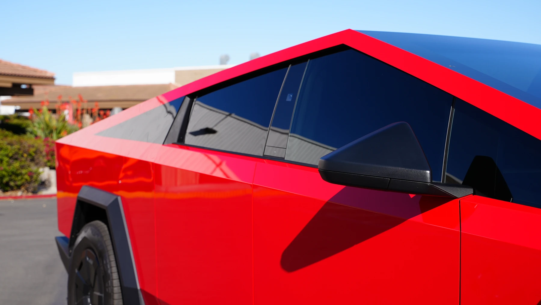 Close-up of a gloss red Tesla Cybertruck wrap with dark windows in a sunny outdoor setting